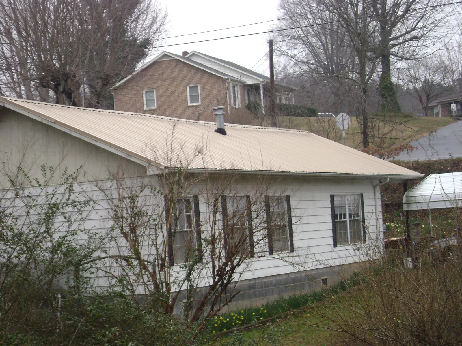 Tan metal roof on a white sided house set into a hillside — Commercial Roofing by Roofing Brothers in Breckenridge